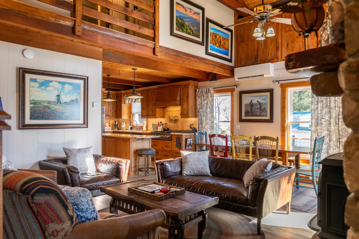 This interior photo captures a spacious open-concept living area featuring plush leather sofas and a wooden dining table. The room feels cozy and inviting, accentuated by decorative artwork on the walls. The kitchen area is visible, seamlessly connected to the main space, creating an environment ideal for family gatherings, relaxing evenings, and shared meals.
