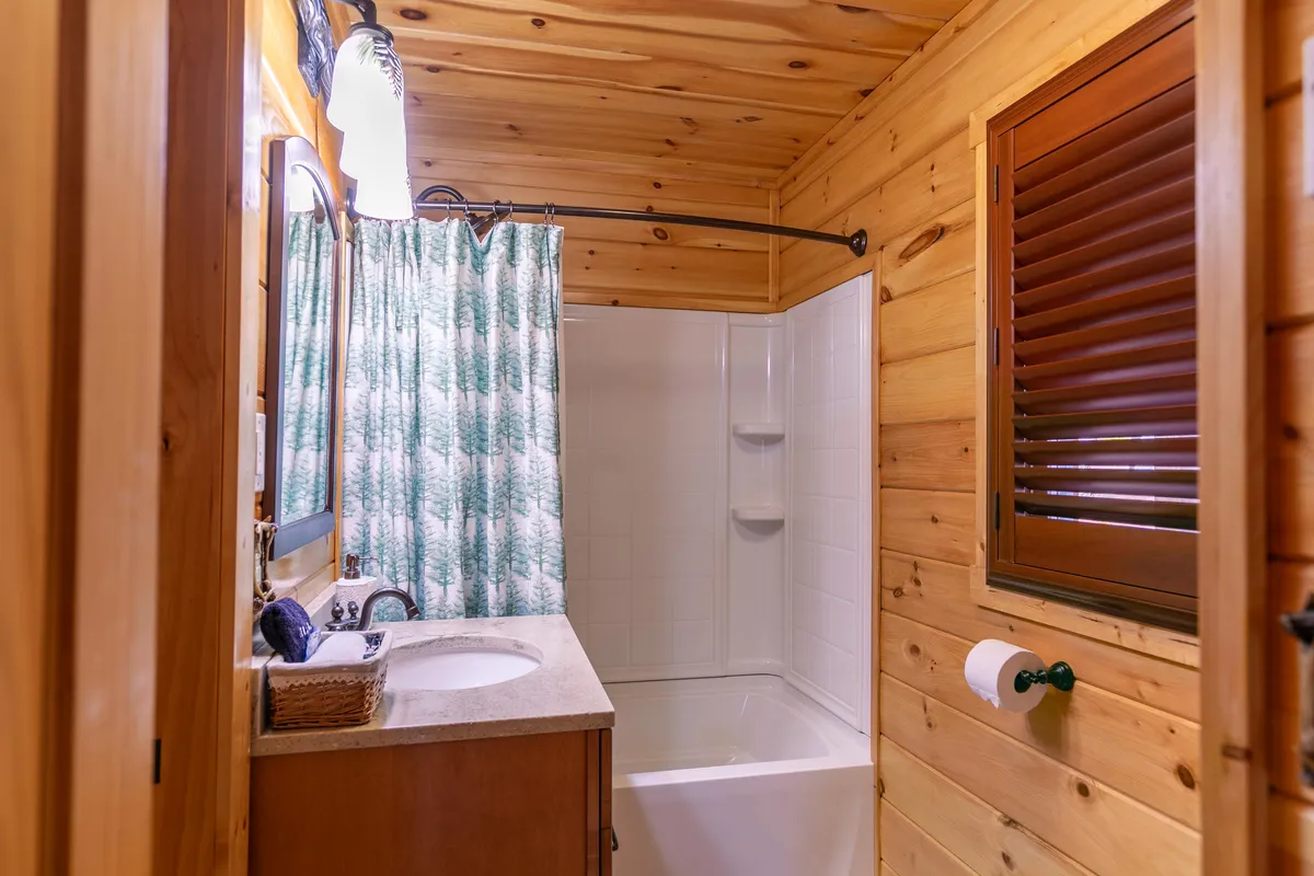 A tranquil bathroom with wood paneling, a bathtub surrounded by soft lighting, a sink, and a shower area with a greenery-patterned curtain. The spa-like atmosphere invites relaxation and rejuvenation after a day outdoors.