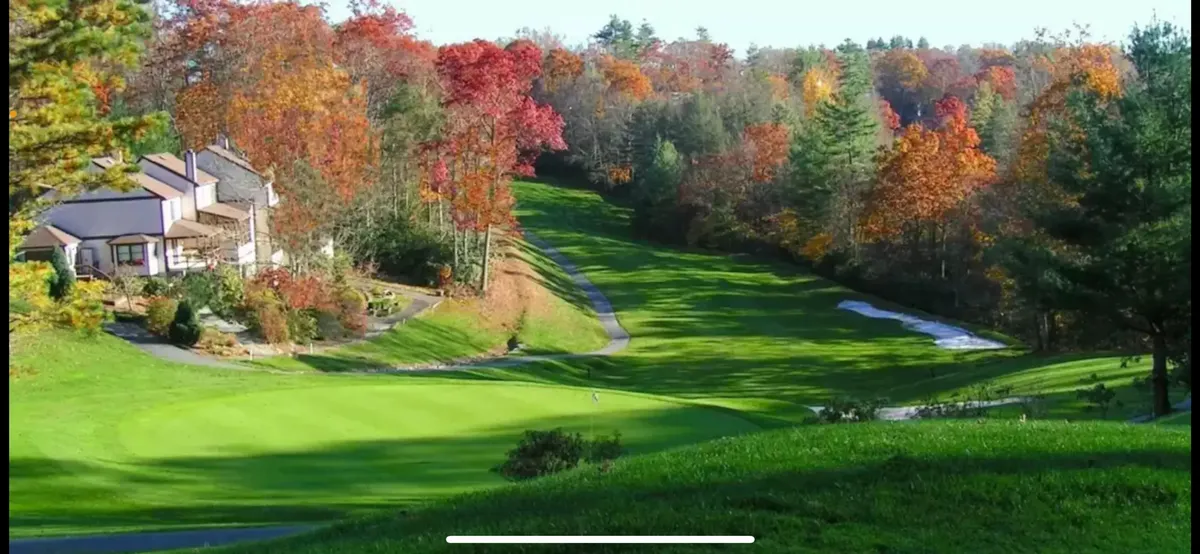 A vibrant exterior view of the lush green golf course set against colorful autumn foliage, with charming homes lining the fairway. The setting is tranquil and inviting, ideal for outdoor gatherings and enjoying the natural beauty of the mountains.