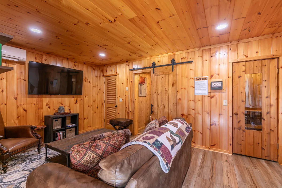 A cozy game room with wood paneling, a plush sofa draped in a patterned throw, a television mounted on the wall, a sliding barn door, and a rug. The inviting setup encourages relaxation, social gatherings, and entertainment, aligning with the section's focus on fun and comfort.