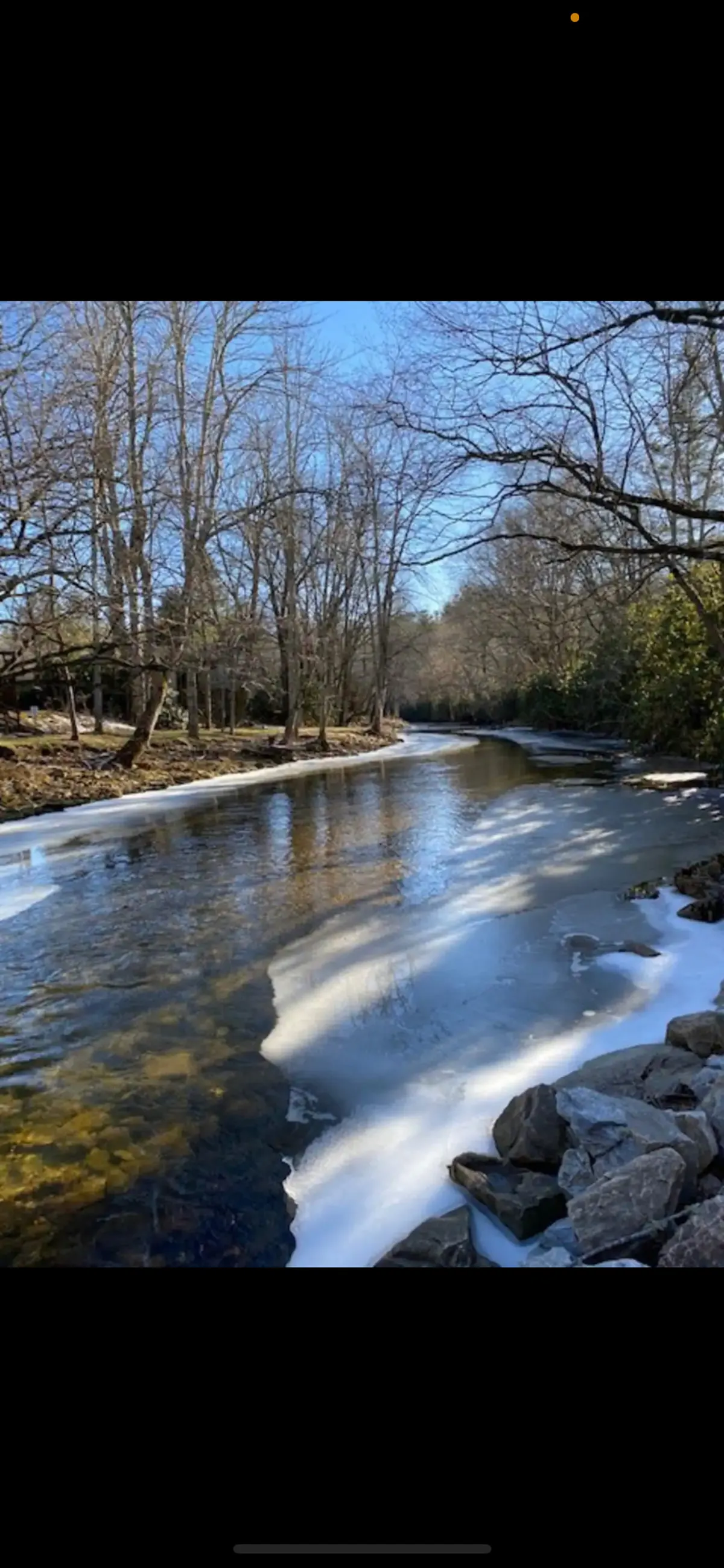 A calm river flanked by a rocky bank and bare trees, with patches of frozen water indicating the transition between seasons. Ideal for fishing, hiking, or quiet reflection, this image showcases outdoor recreation beyond summer months.