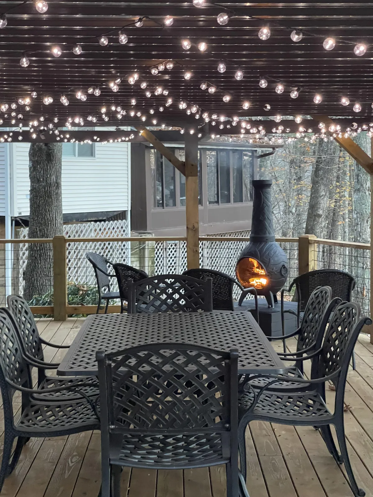 An inviting outdoor dining area lit with string lights, featuring an outdoor table and a fireplace. The setting is cozy and romantic, ideal for evening dinners or gathering with loved ones under the stars.