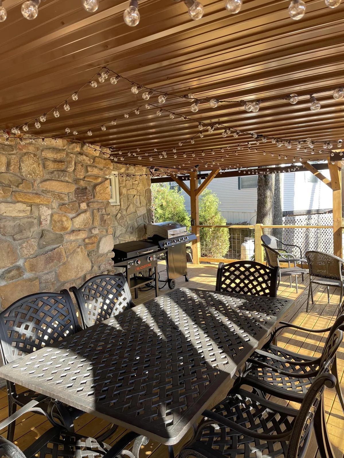 An outdoor dining table sits under glowing string lights next to a gas grill, with comfortable chairs arranged for group gatherings. The scene feels festive yet relaxed, perfect for evening barbecues or al fresco dining after a day in the mountains.
