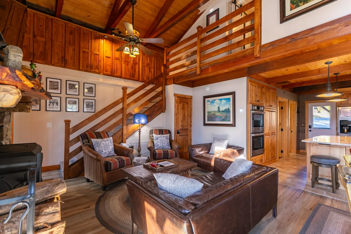 An inviting interior scene featuring a comfortable sofa set, a central fireplace, a glimpse of the kitchen island, and tasteful artwork. The open arrangement encourages conversation and shared experiences, making the space ideal for family interaction and entertaining guests.