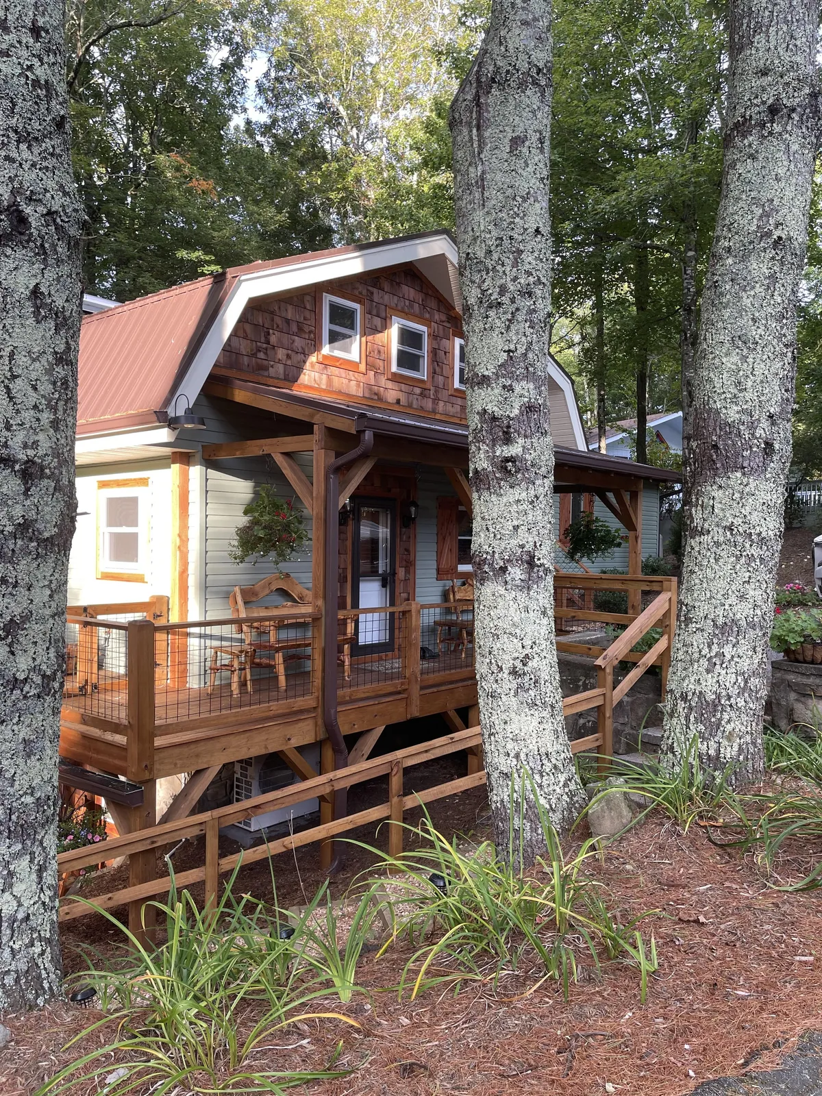 A charming wooden porch adorned with decorative stonework, lush greenery, and rustic architecture. The scene conveys an inviting outdoor space perfect for morning coffee, dining, or relaxing with friends while overlooking the natural surroundings.