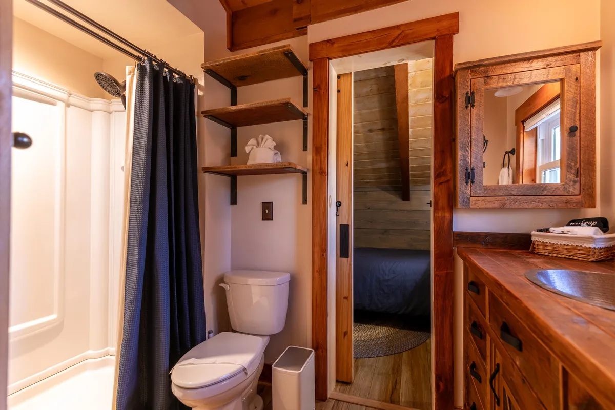 A stylish bathroom with a wooden countertop, mirrored cabinet, and shower area separated by a dark curtain. The space is intimate and inviting, perfect for refreshing after a sauna session or outdoor adventure.